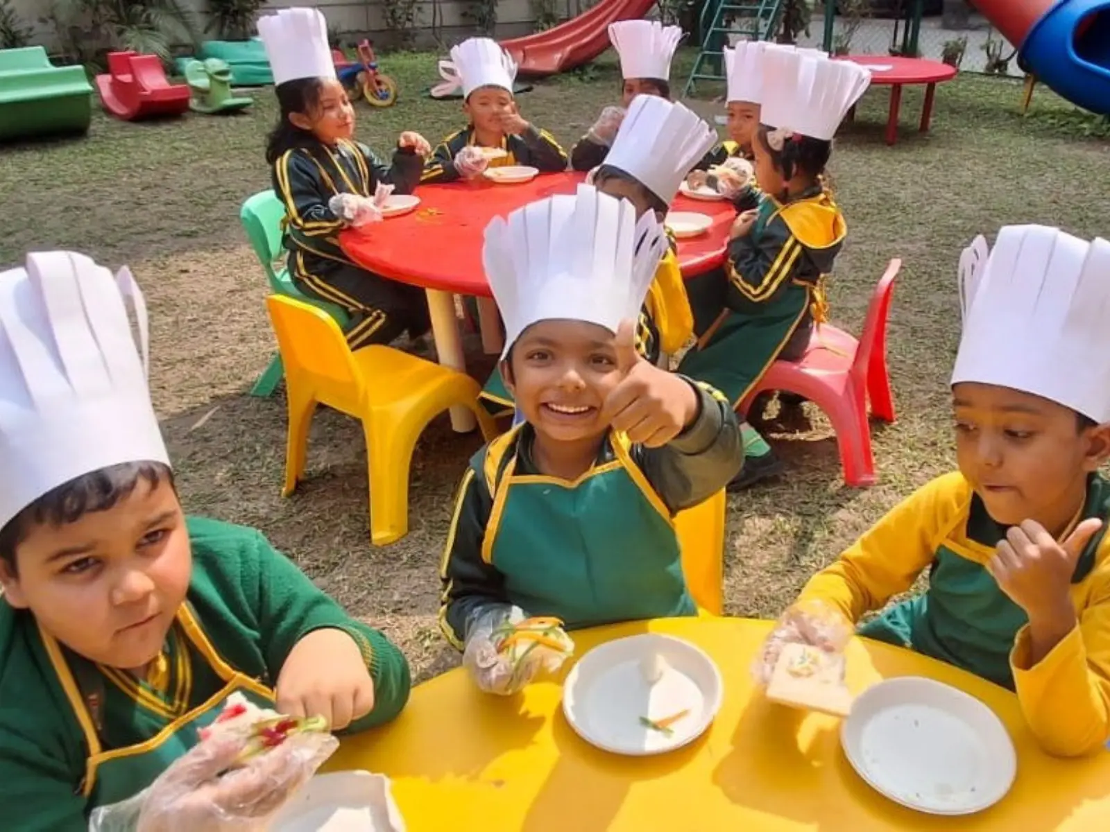 Preschool students at Kidz Paradize wearing chef hats and aprons during an outdoor activity-based cooking session in the play area